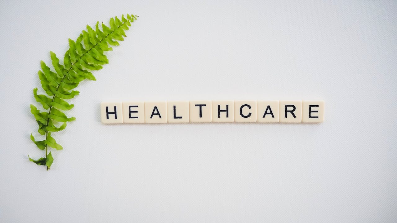 about-01 Healthcare word spelled with Scrabble tiles next to a green fern leaf on a white background.
