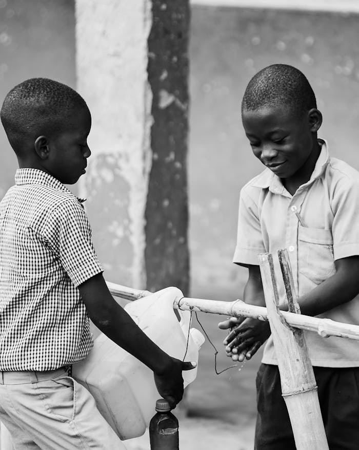 Two children washing hands at an outdoor water station in Ghana.